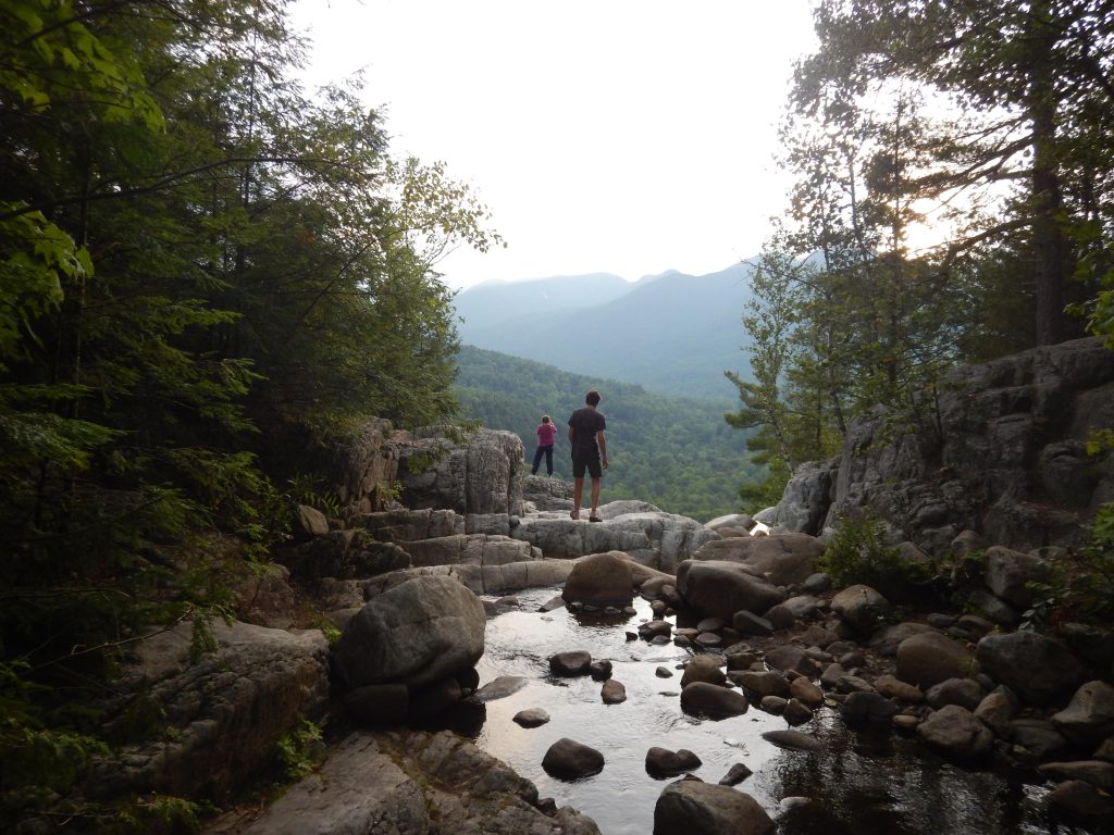 Two individuals stand on rocks in the middle of a river. 