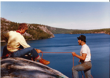 Two individuals hold on to a rope at the side of a waterfront. 