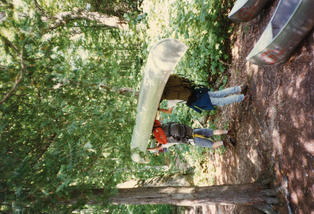 two individuals portage a canoe.