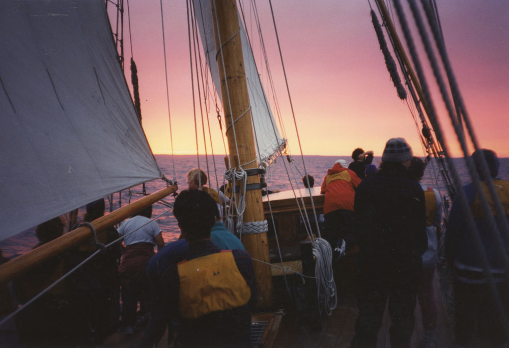 The sun sets on the sailboat.