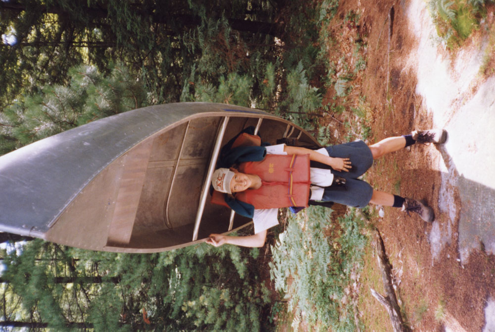 An individual portages a canoe alone.